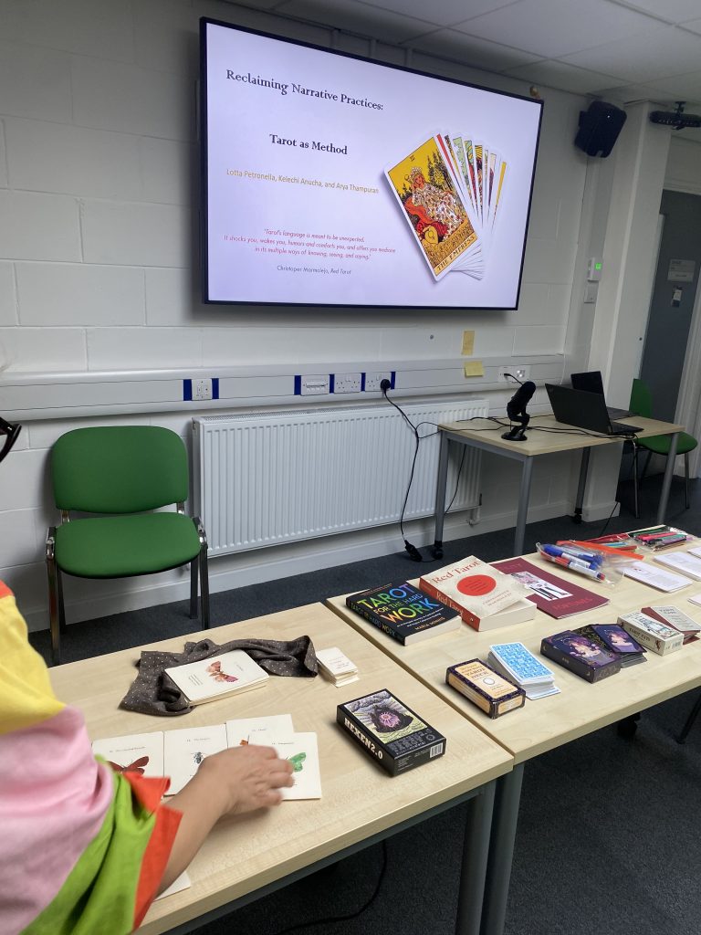 Photograph of a visualiser screen showing slides for the 'Tarot as Method' event. In front of the visualiser is a table with decks of tarot cards and books laid out.