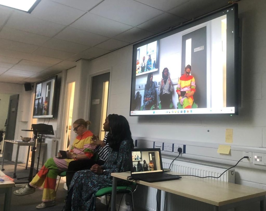 Photograph of two speakers sitting in front of a visualiser screen, in a University building.